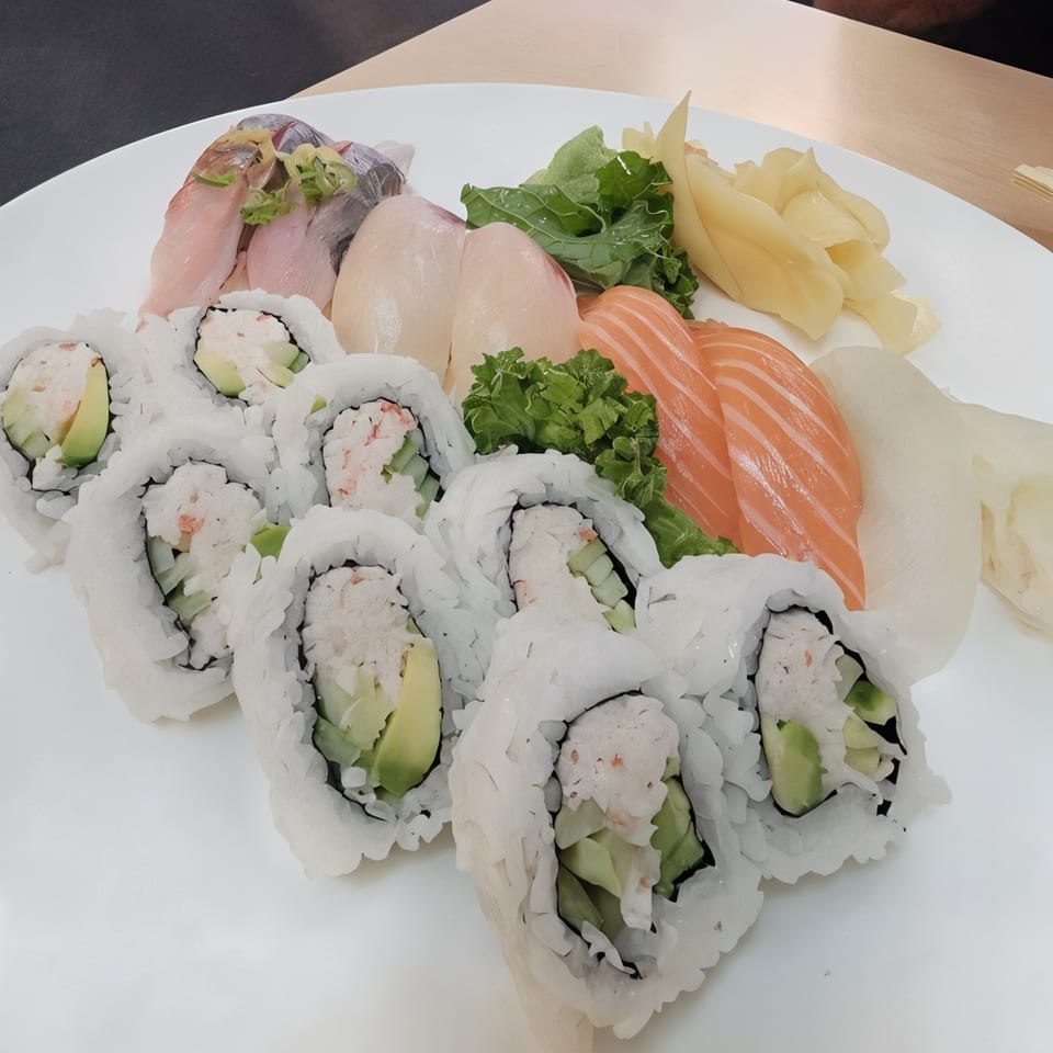 A white platter of Sushi Bei's sushi rolls, sashimi, and nigiri, garnished with ginger and greens.