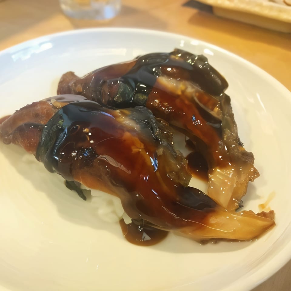 Two pieces of dark, glossy eel sushi with sweet sauce on a white plate at Sushi Bei.