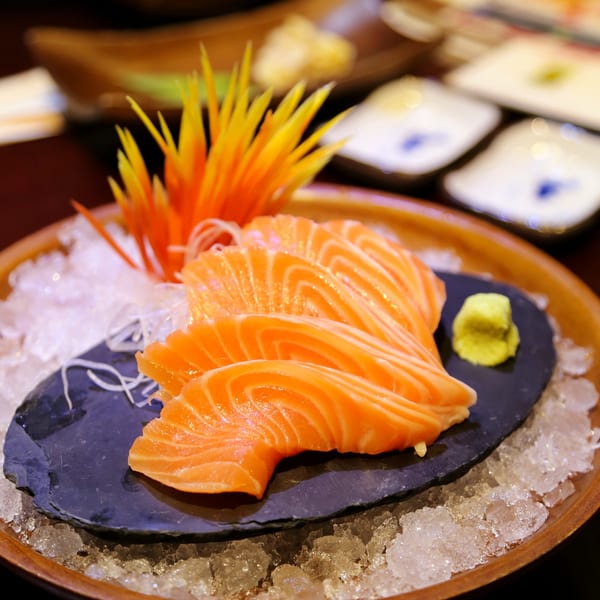 Fresh salmon sashimi slices with wasabi and shredded daikon on a slate plate over ice.