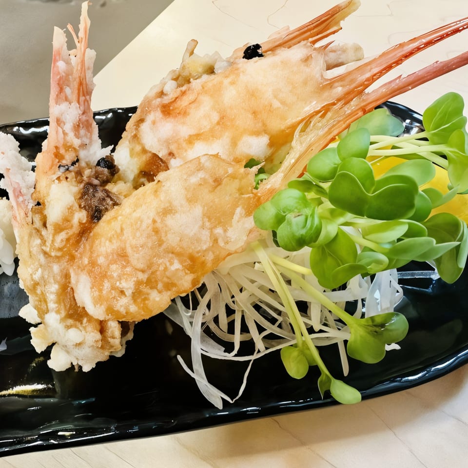 Two large, golden-fried tempura shrimp with microgreens and shredded daikon on a black plate.