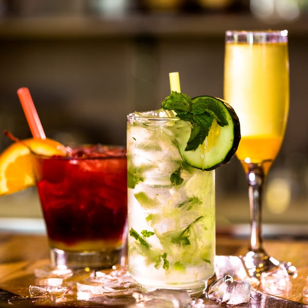 Three vibrant cocktails, including a mojito with cucumber and mint, on a bar with ice.
