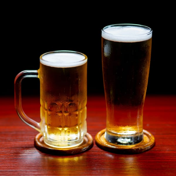 Two frosty glasses of beer, a mug and a pilsner, on wooden coasters at Sushi Bei.